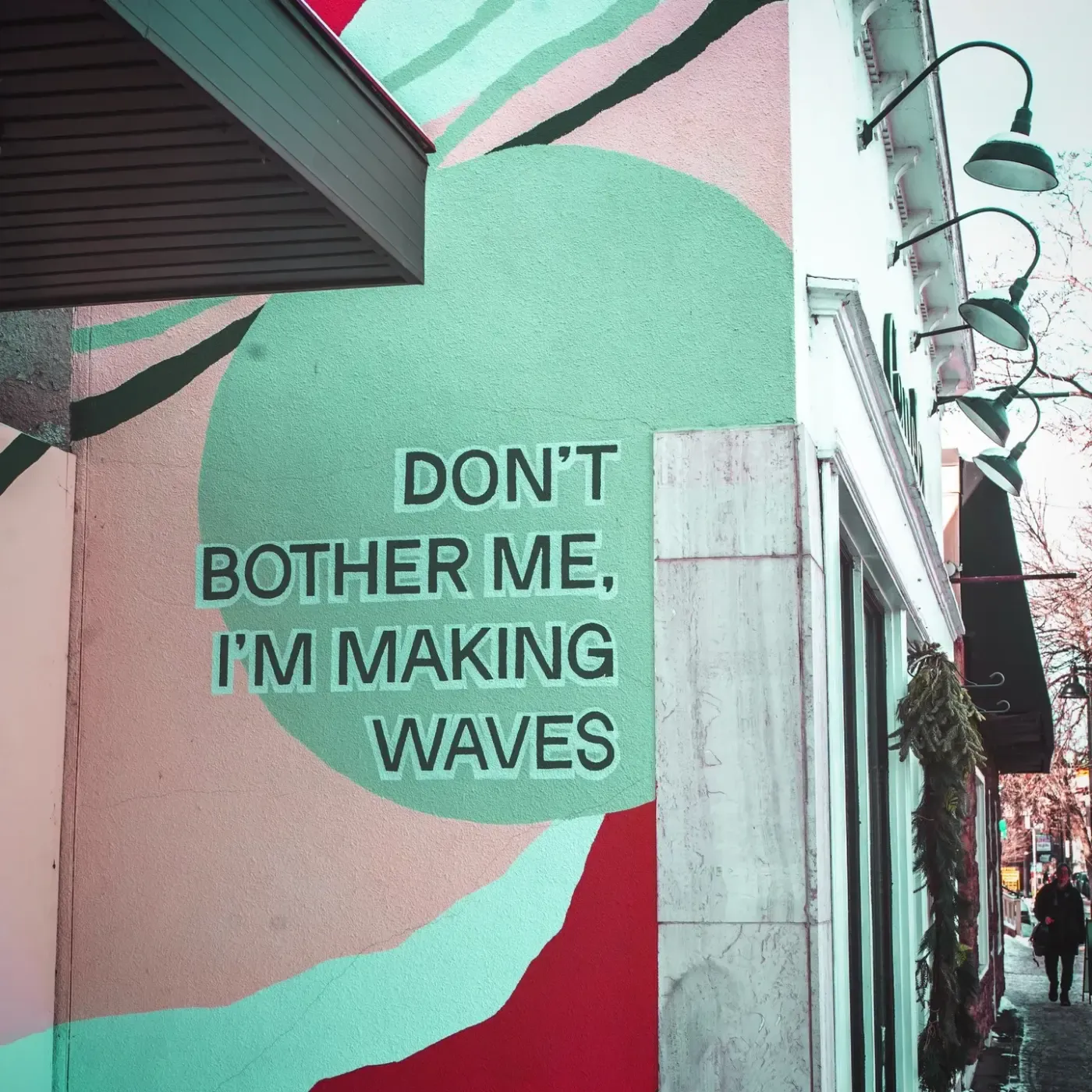 A painted wall mural reading Don't bother me, I'm making waves, on a street corner