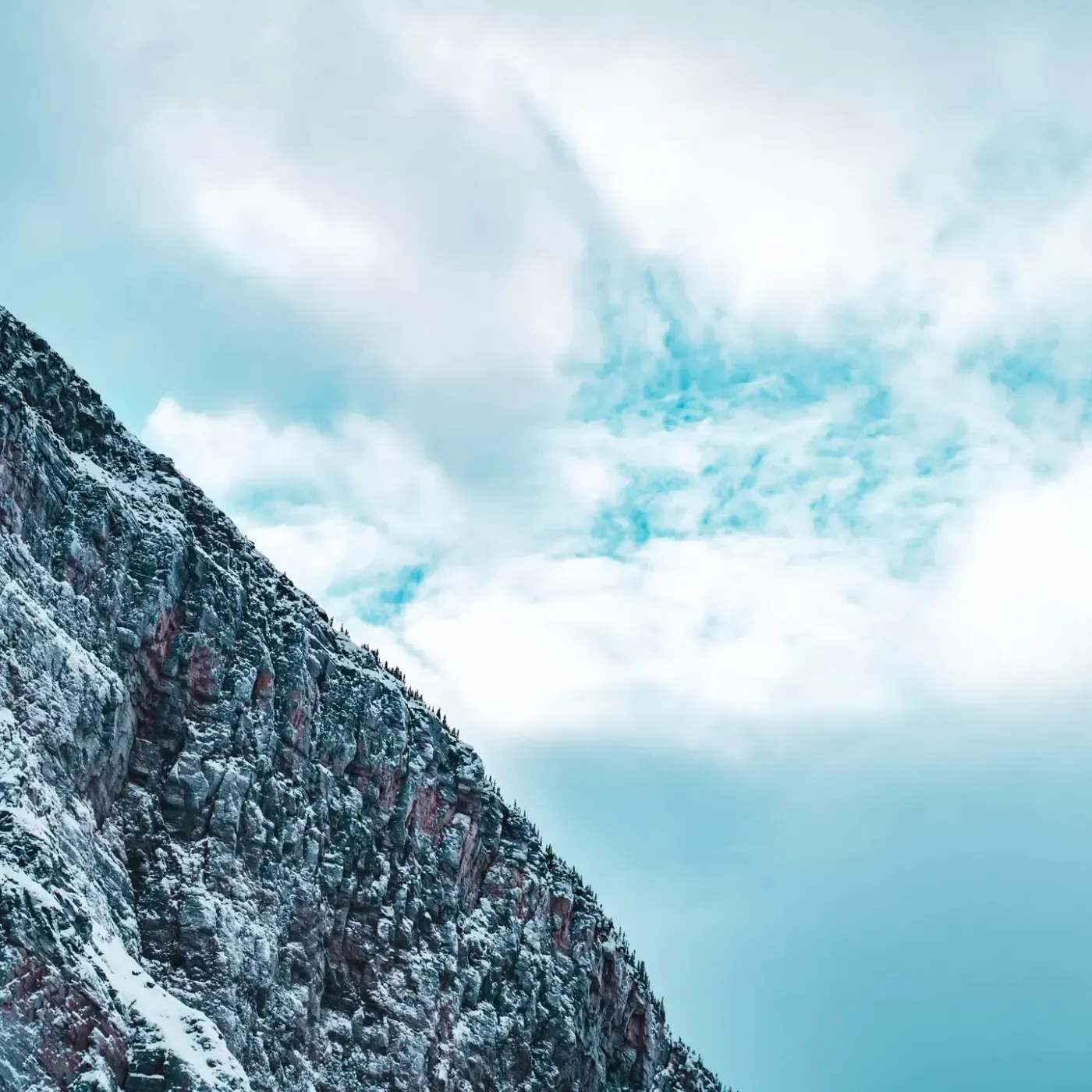 A steep rock face streaked with pale blue ice against an overcast sky