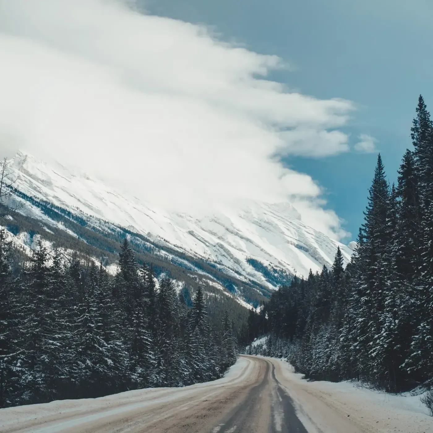 A snow-covered road running towards a mountain wall under low cloud