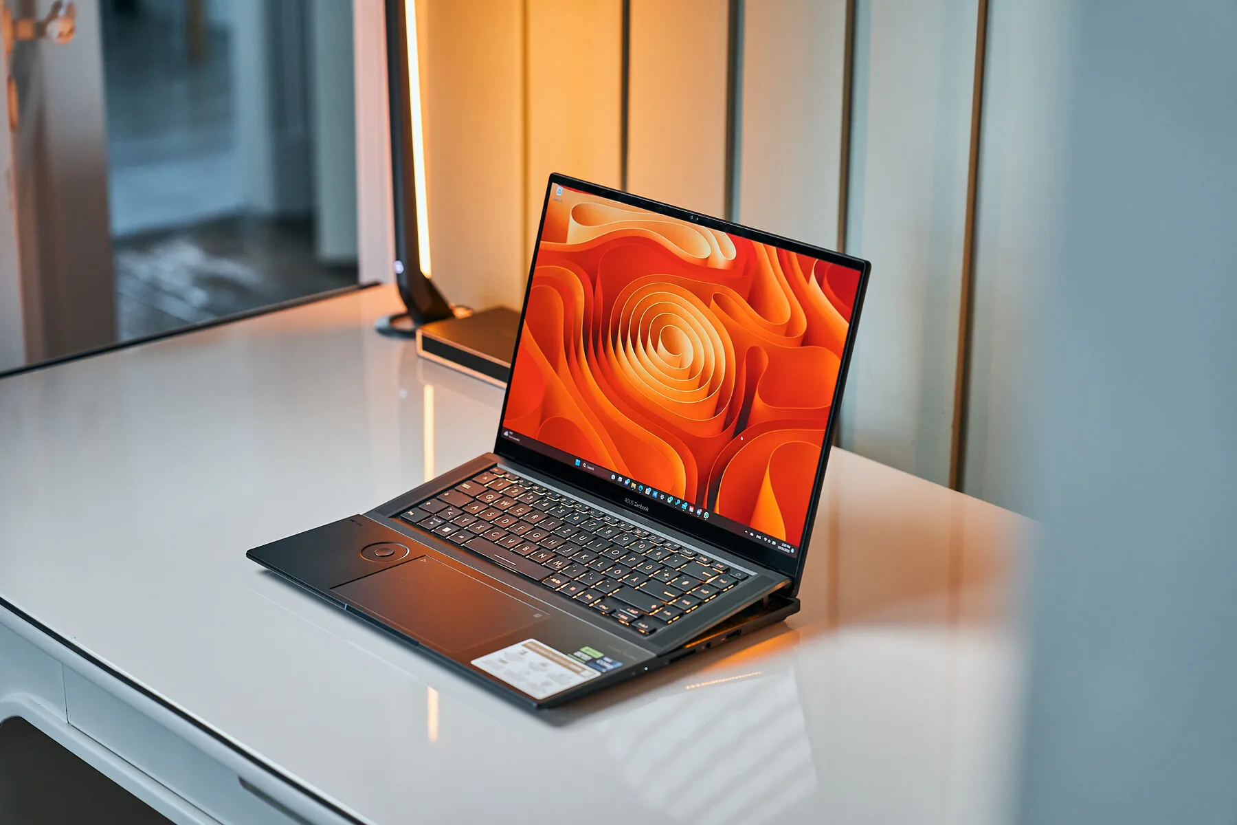 An Asus Zenbook Pro 16X OLED open on a white desk, with its keyboard deck raised at the back